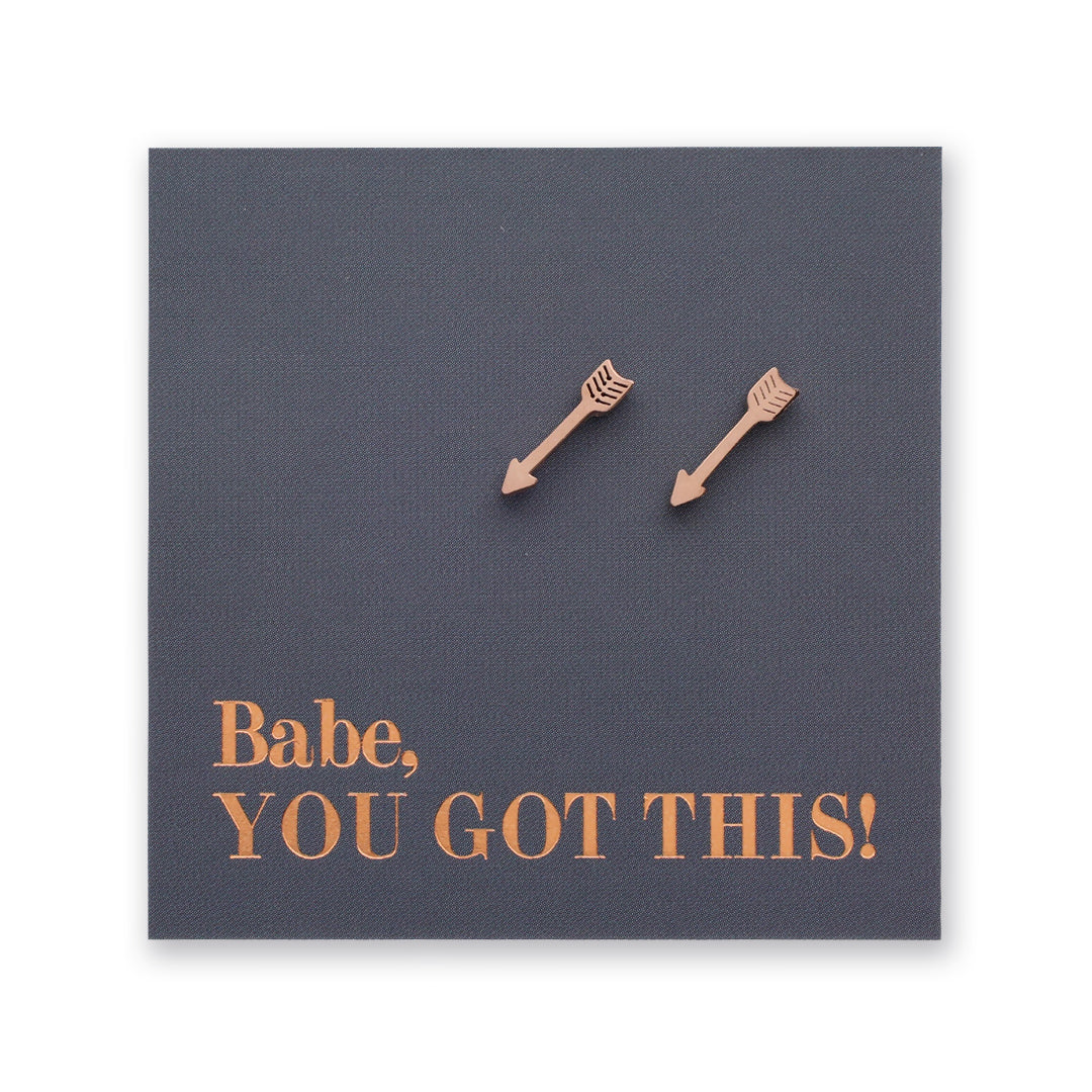 Two rose gold arrow-shaped stud earrings displayed on a dark gray square card with the text 'Babe, YOU GOT THIS!' in rose gold lettering, set against a plain white background.