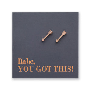 Two rose gold arrow-shaped stud earrings displayed on a dark gray square card with the text 'Babe, YOU GOT THIS!' in rose gold lettering, set against a plain white background.
