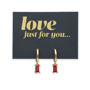 A pair of gold huggie hoop earrings with rectangular pink gemstones, displayed on a dark charcoal card that reads 'love just for you.
