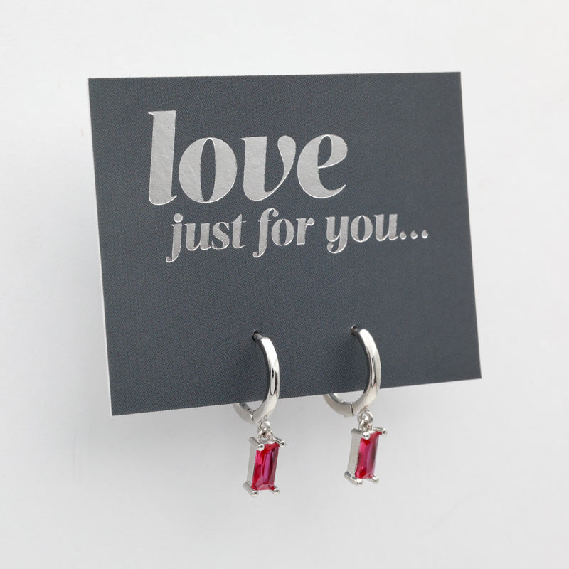 A pair of silver huggie hoop earrings with rectangular red gemstones, displayed on a dark gray card that reads 'love just for you.