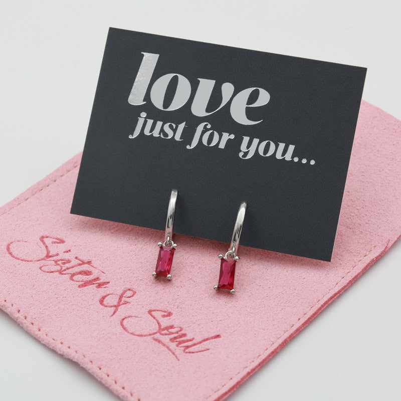A pair of silver drop earrings with rectangular pink gemstones, displayed on a black card that reads 'love just for you.