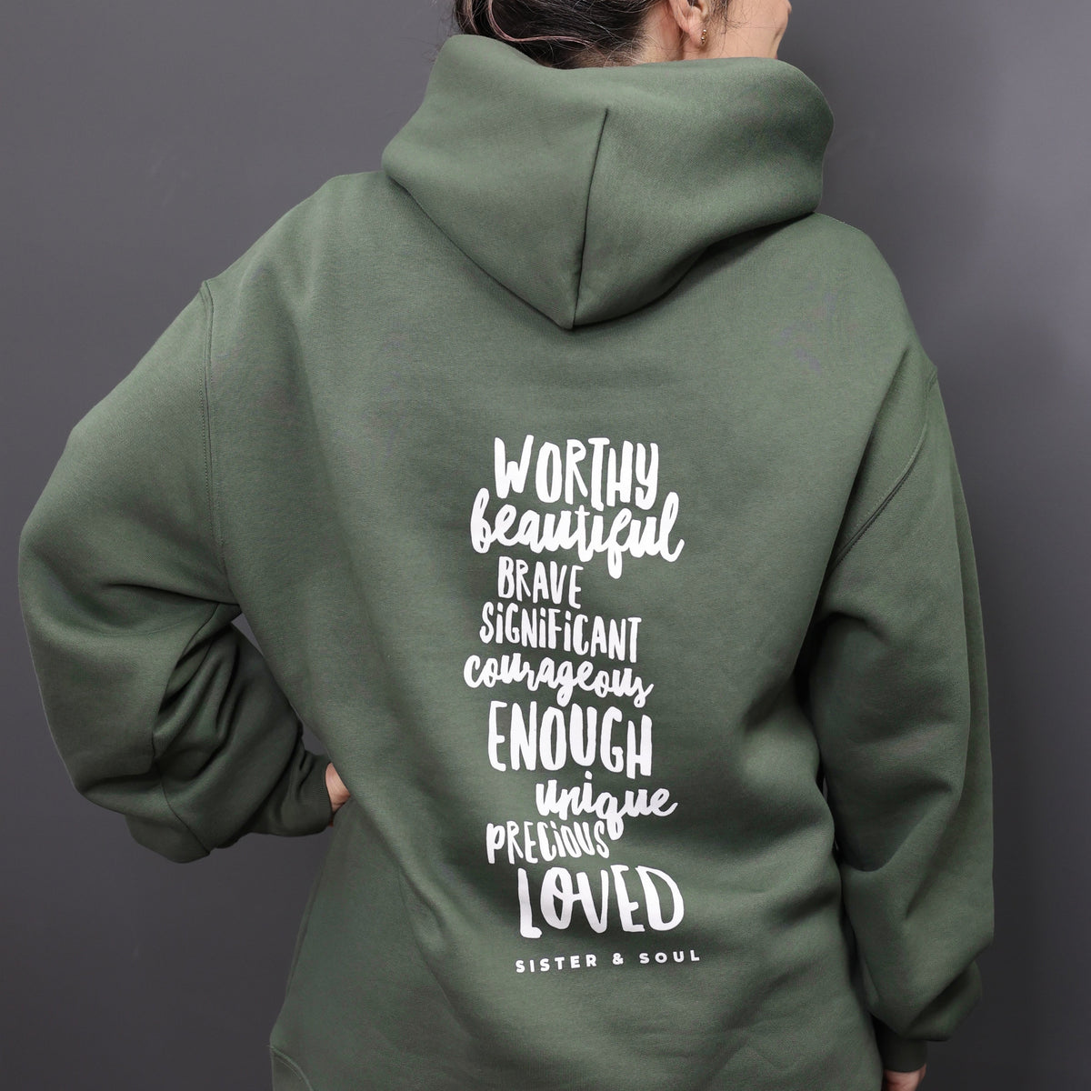 Person wearing a green hoodie with motivational text on the back against a gray background