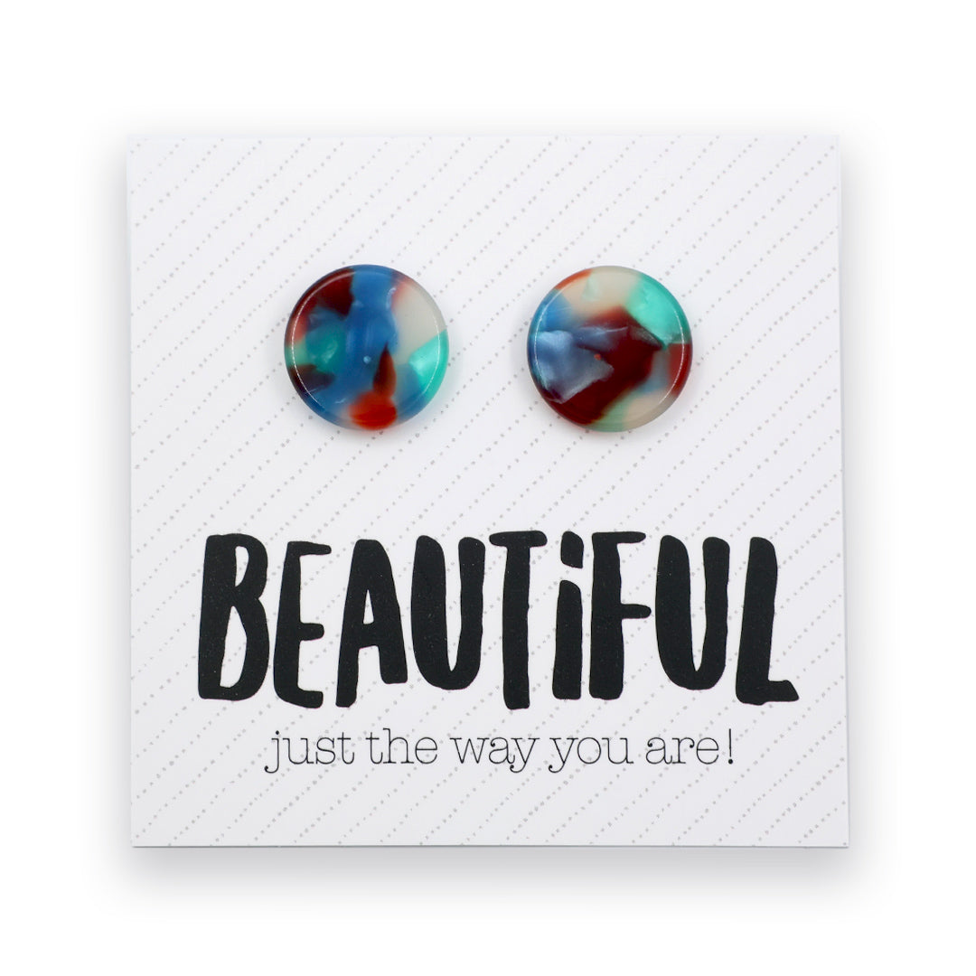 A pair of round marbled stud earrings in blue, red, and teal tones, displayed on a white textured card with the text 'BEAUTIFUL just the way you are!' below them.