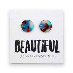 A pair of round marbled stud earrings in blue, red, and teal tones, displayed on a white textured card with the text 'BEAUTIFUL just the way you are!' below them.