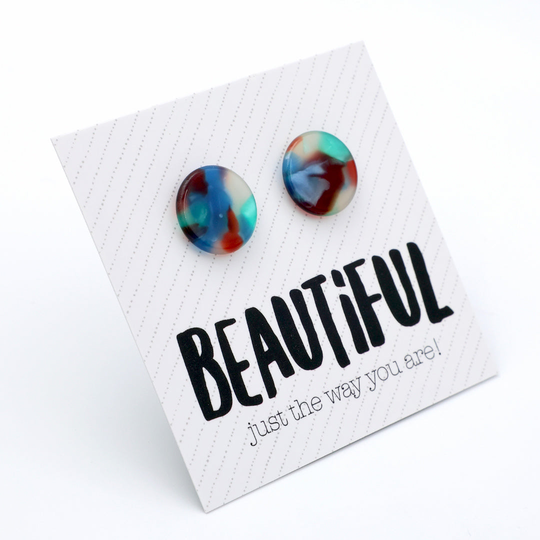 A pair of round marbled stud earrings in blue, red, and teal tones, displayed on a white textured card with the text 'BEAUTIFUL just the way you are!' below them.