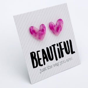A square white card with diagonal dotted lines, featuring two pink marbled heart-shaped earrings attached near the top and the word 'BEAUTIFUL' in large black letters, with smaller text reading 'just the way you are!' below.