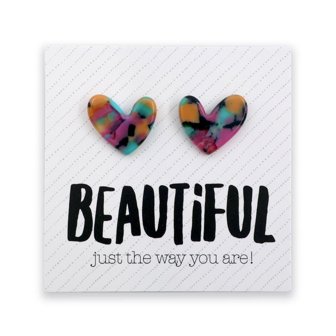 A pair of heart-shaped stud earrings with a colorful marbled pattern in orange, yellow, blue, green, and pink, displayed on a white square card that reads 'BEAUTIFUL just the way you are!'.