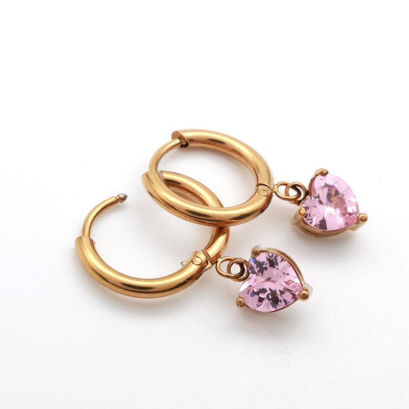 A pair of gold hoop earrings with dangling heart-shaped pink gemstones, displayed on a clean white background.