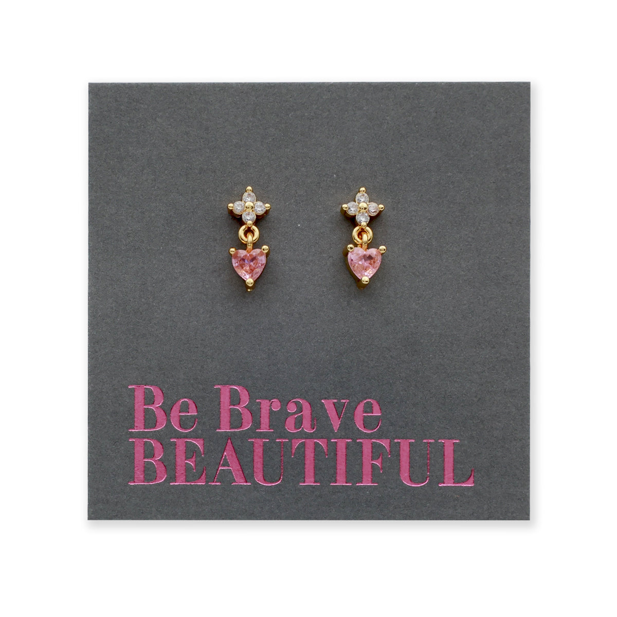 A pair of gold dangle earrings with small clear stones at the top and pink heart-shaped stones below, displayed on a dark gray backing card that reads 'Be Brave BEAUTIFUL' in pink text.