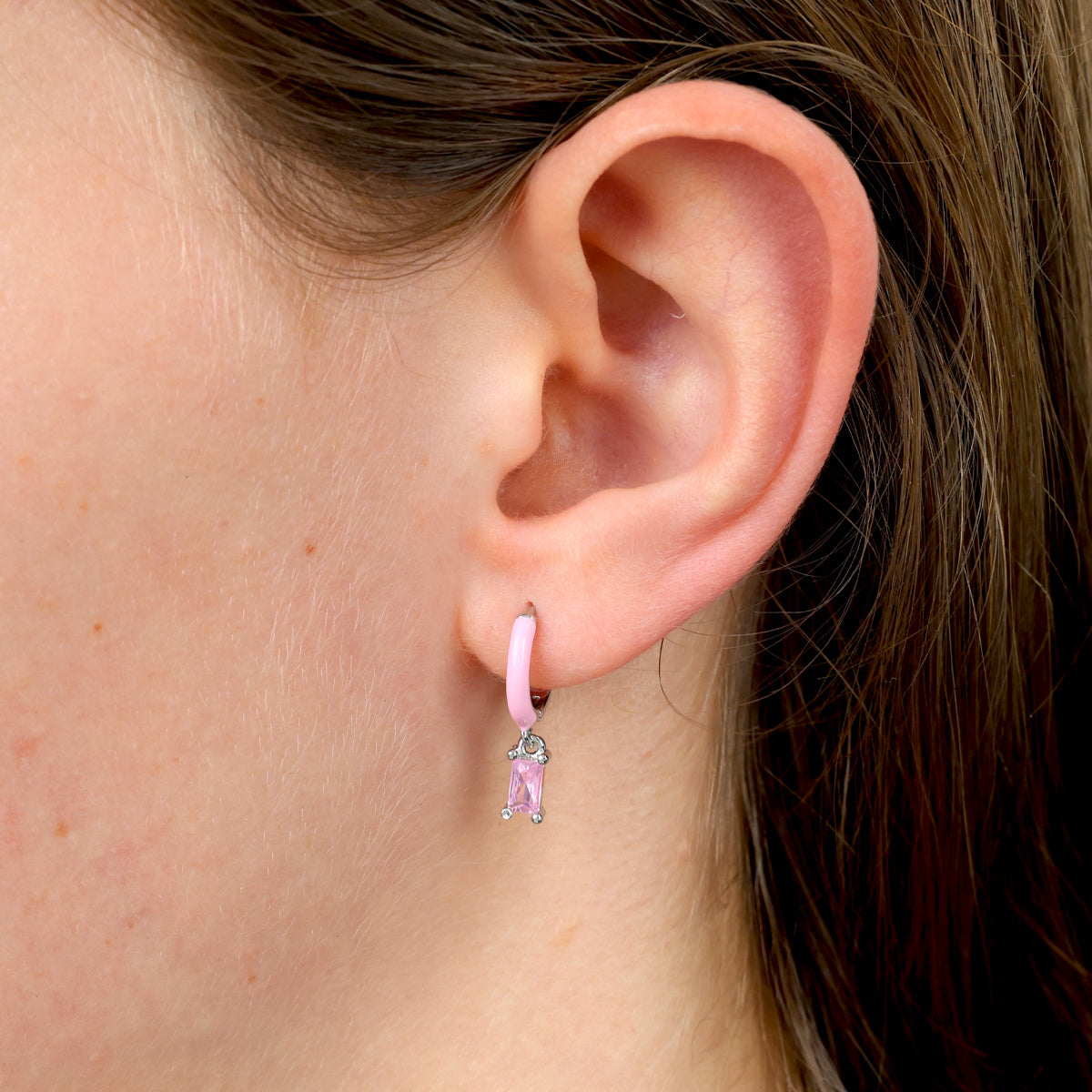 Close-up of an ear wearing a pink hoop earring with a clear gemstone.