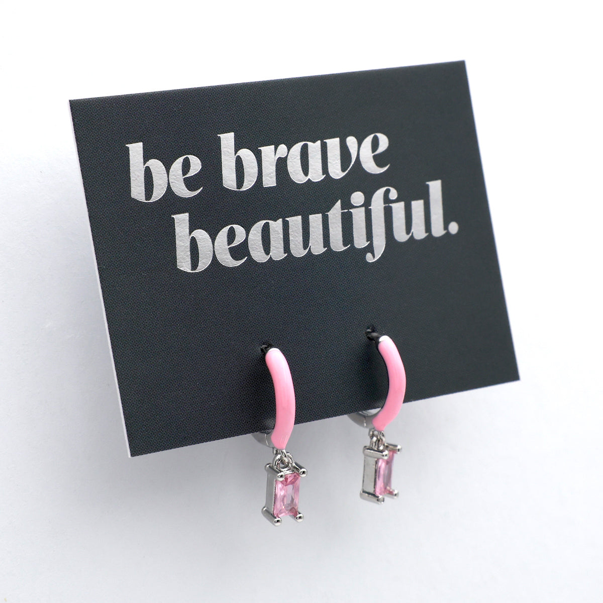 Pink earrings on a card with 'be brave beautiful' text on a white background