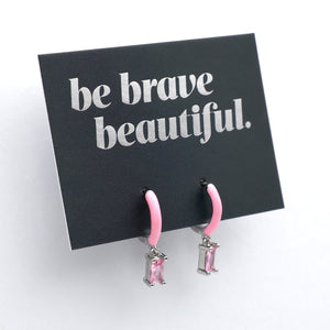 Pink earrings on a card with 'be brave beautiful' text on a white background
