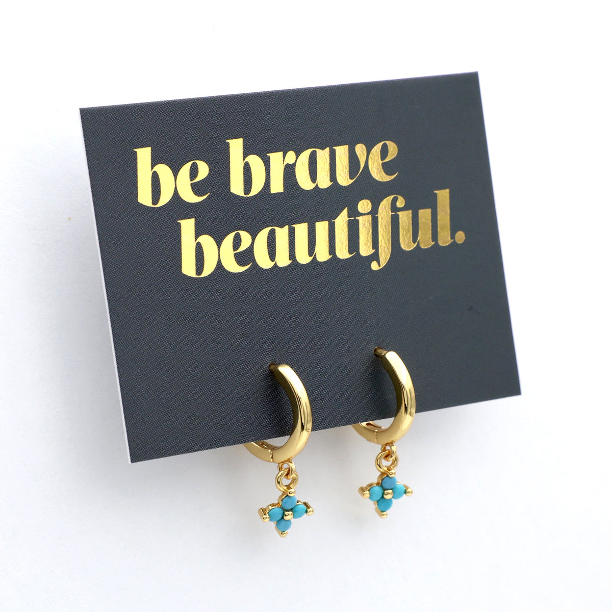 Gold hoop earrings with turquoise charms on a 'be brave beautiful' card.