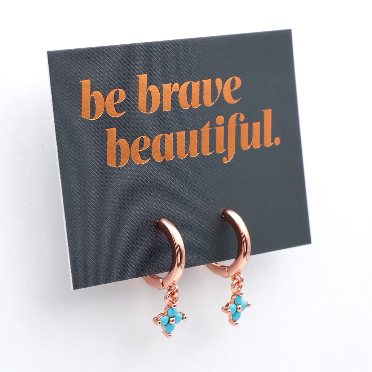 Rose gold earrings with turquoise charms on a card that says 'be brave beautiful'.