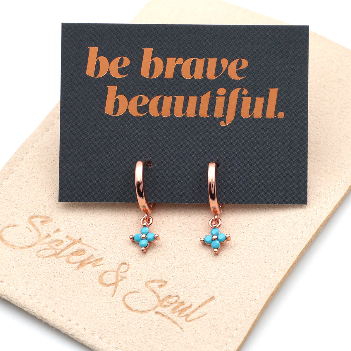 Rose gold earrings with turquoise stones on a 'be brave beautiful' card, brand 'Sister & Soul' visible.