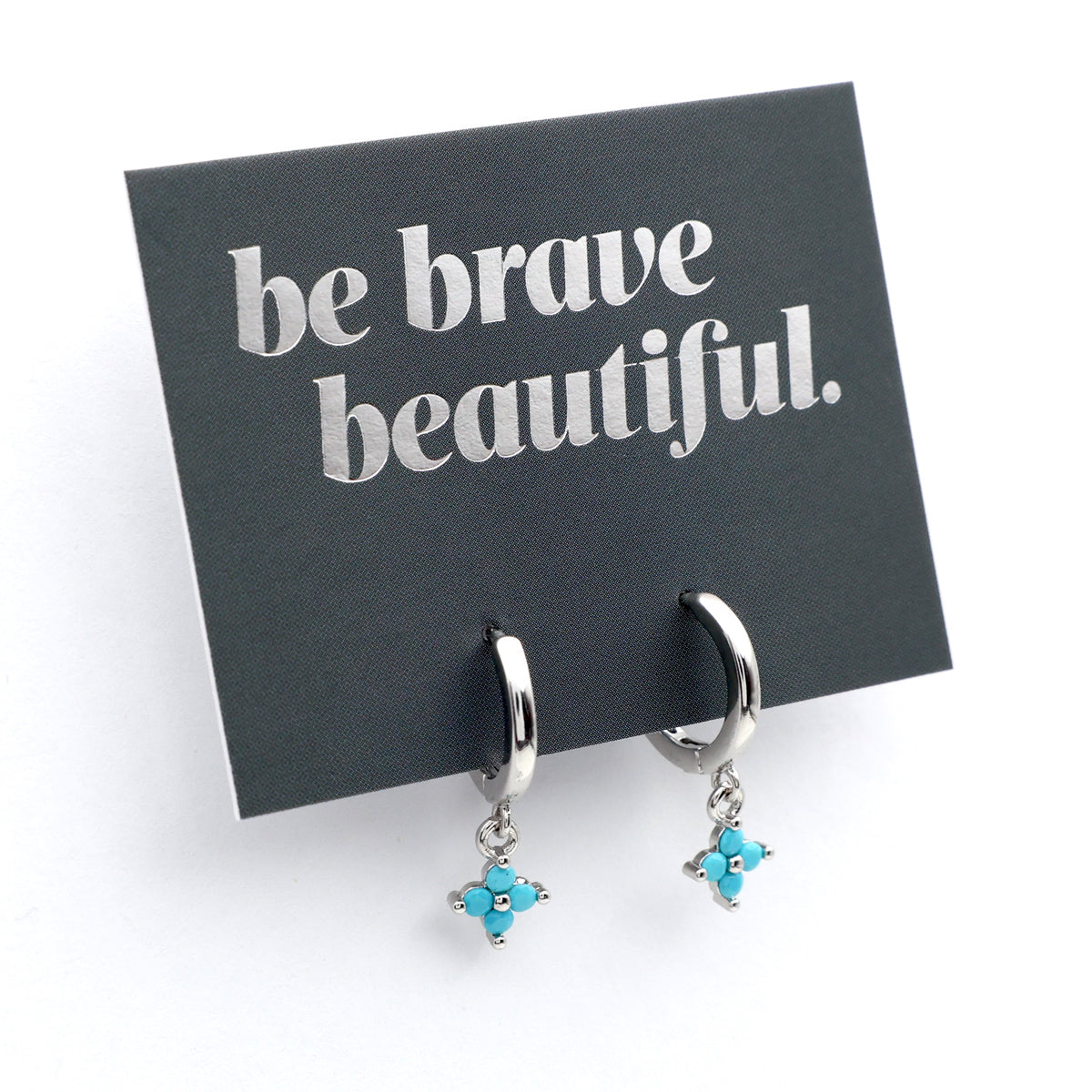 Silver earrings with turquoise stones on a card with 'be brave beautiful' text.