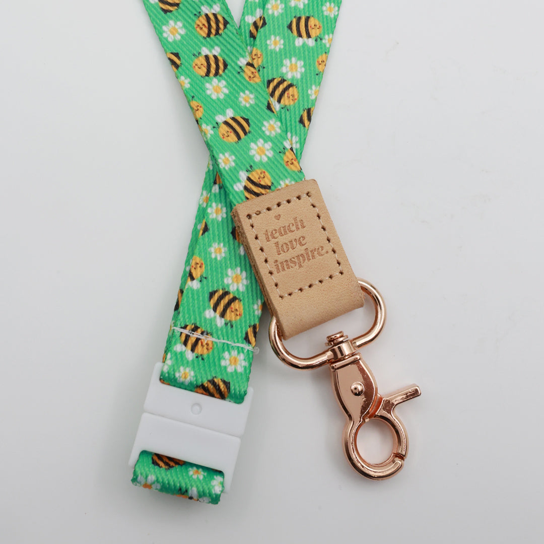 Teach Love Inspire embossed on a green bee and daisy lanyard with tan trim and a lobster clasp.