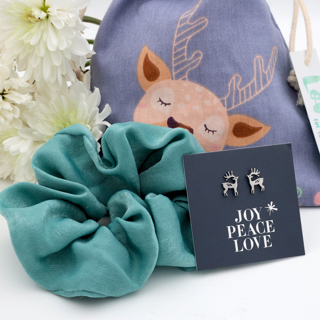 Teal scrunchie, drawstring bag with deer design, and 'Joy Peace Love' card on a white background