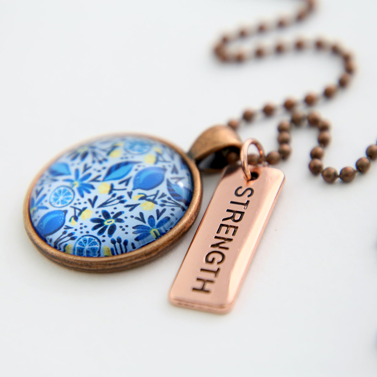 Necklace with floral pendant and 'STRENGTH' tag on a white background