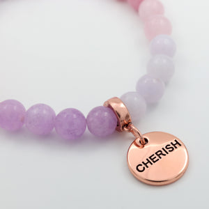 Purple beaded bracelet with a rose gold charm displaying the word 'CHERISH' on a light background