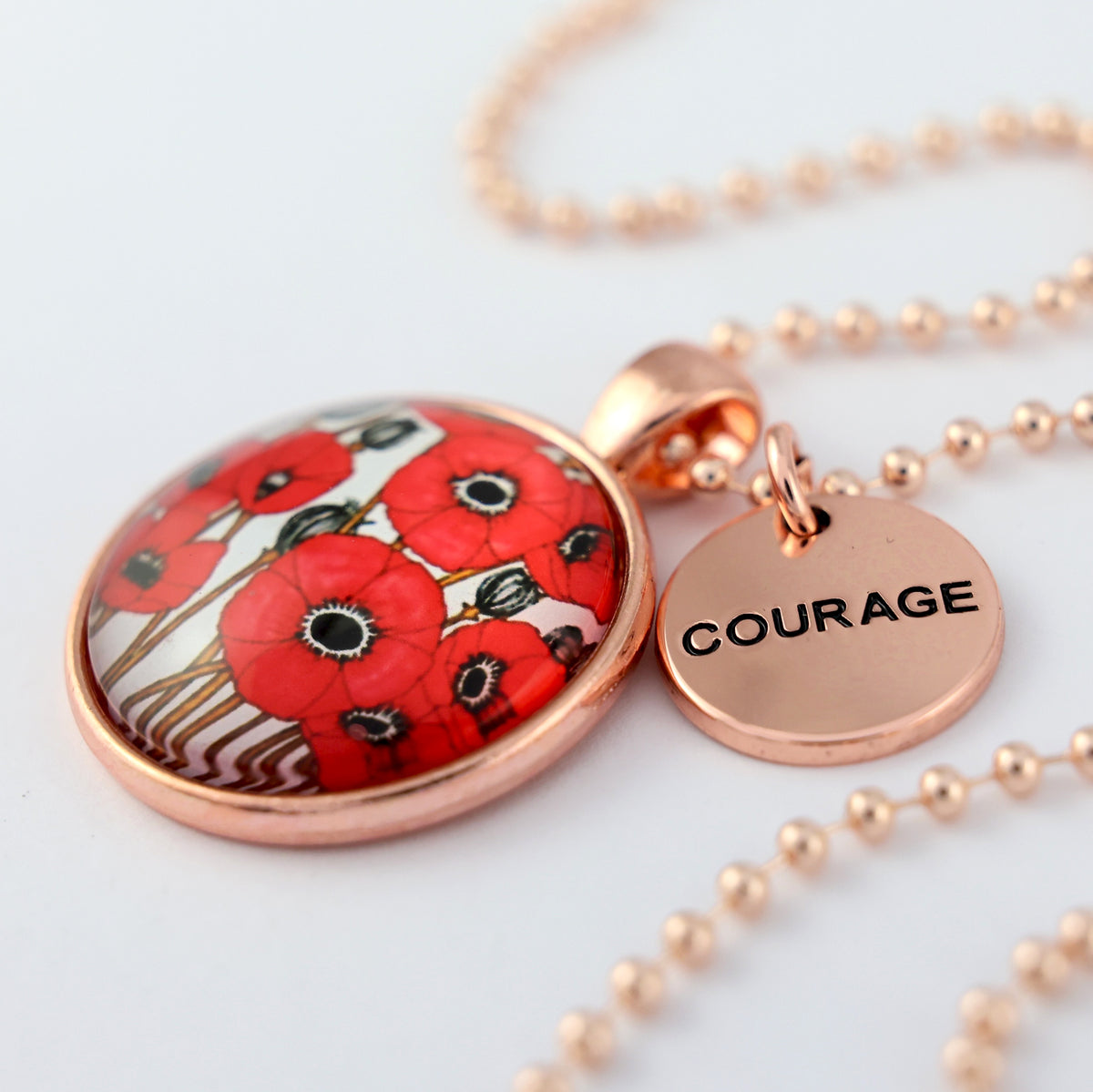 Necklace with red poppy design pendant and 'COURAGE' tag on a white background