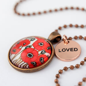Necklace with a pendant featuring red poppies and a round tag with 'LOVED' on a white background.