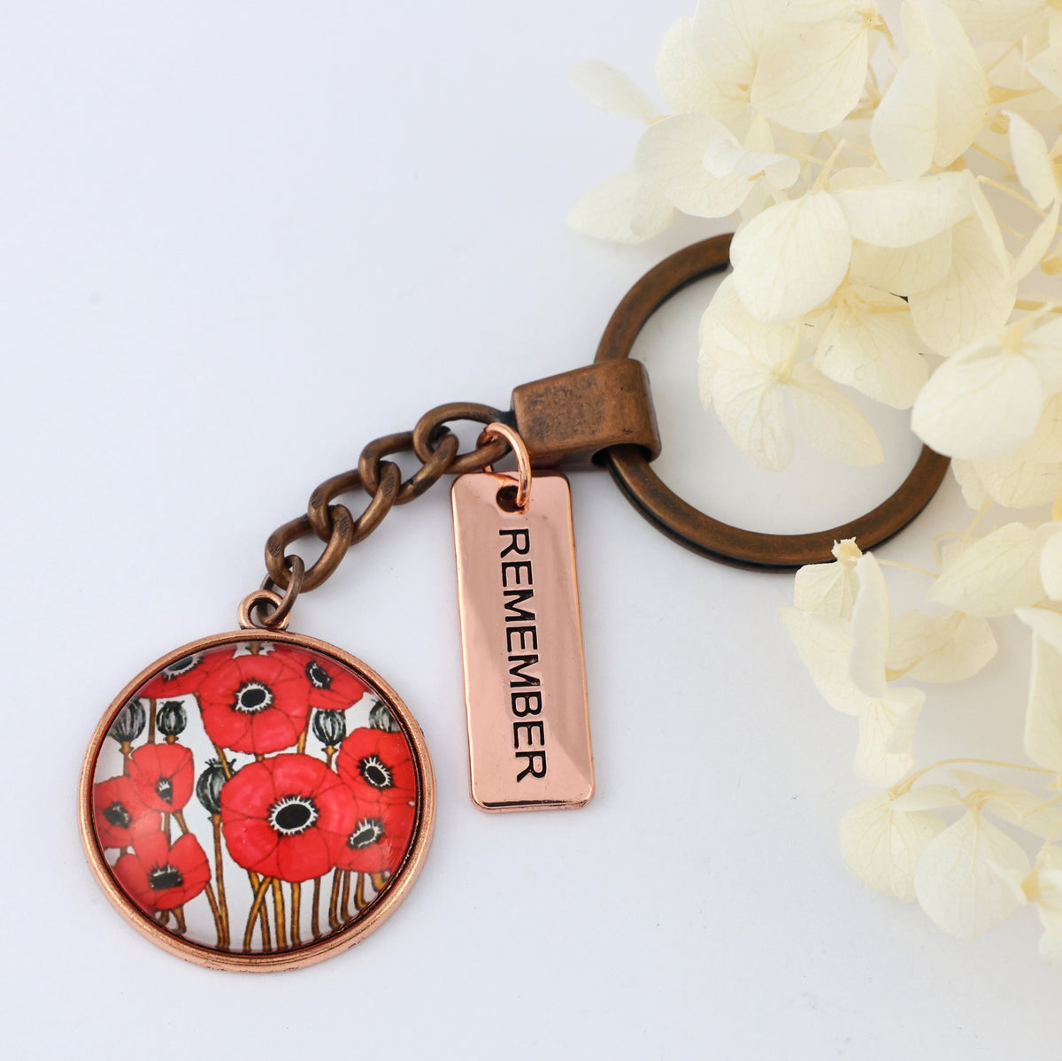 Keychain with poppy design and 'REMEMBER' tag on a white background
