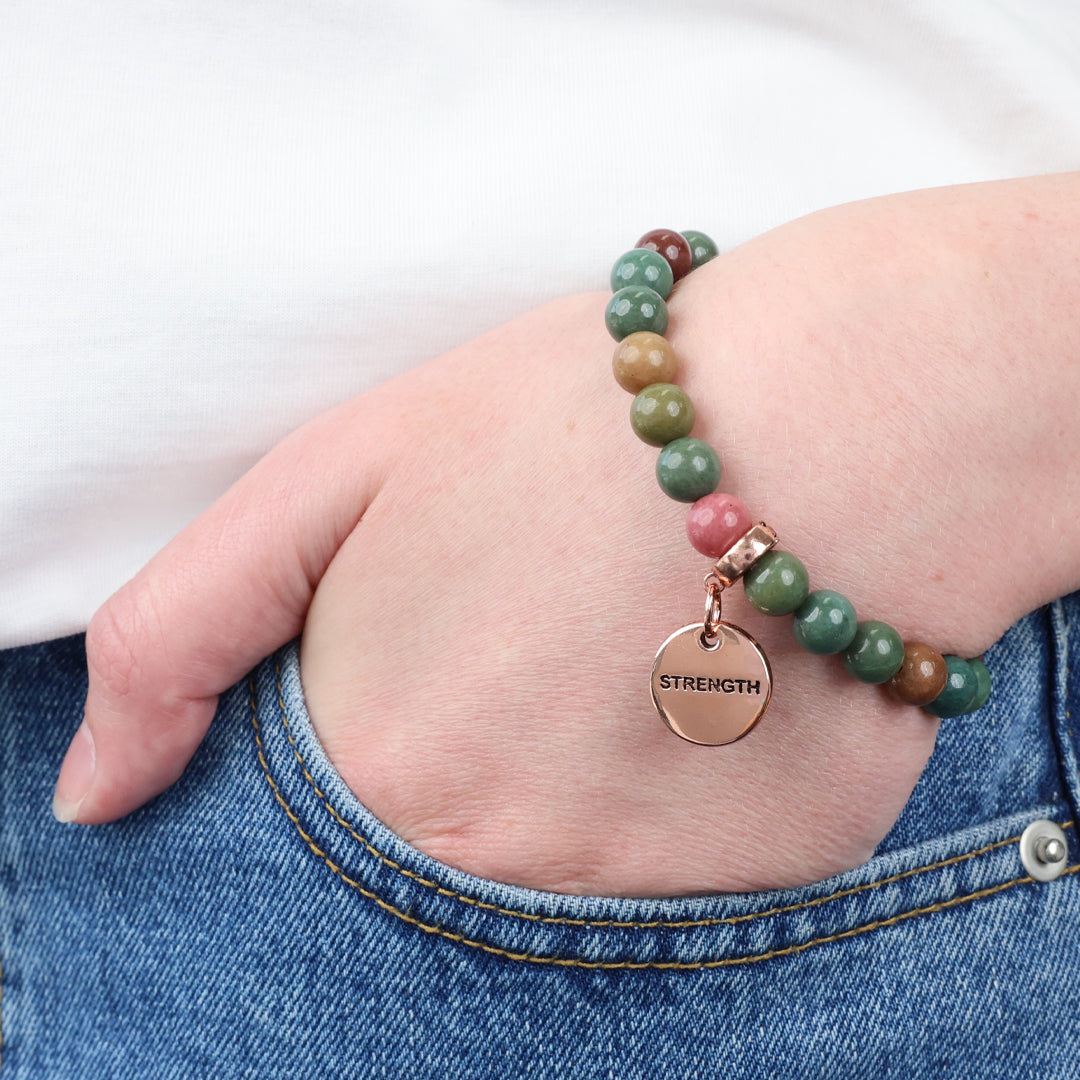Bracelet with 'STRENGTH' charm on a wrist, worn with jeans.