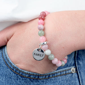 Bracelet with pink and green beads and a 'FAMILY' charm on a wrist.