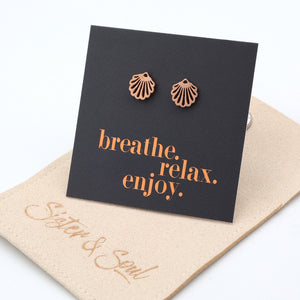 Rose gold shell earrings on a black card with 'breathe. relax. enjoy.' text, on a beige surface.