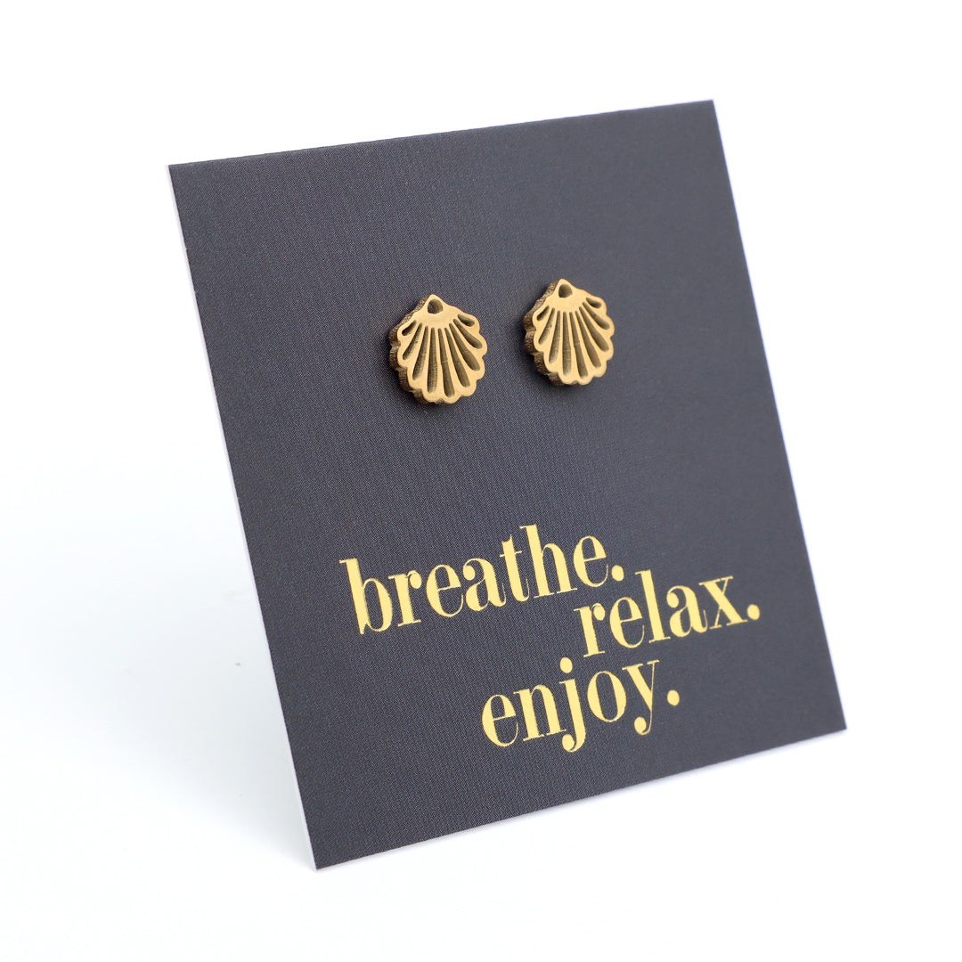 Gold shell-shaped earrings on a black card with 'breathe. relax. enjoy.' text.