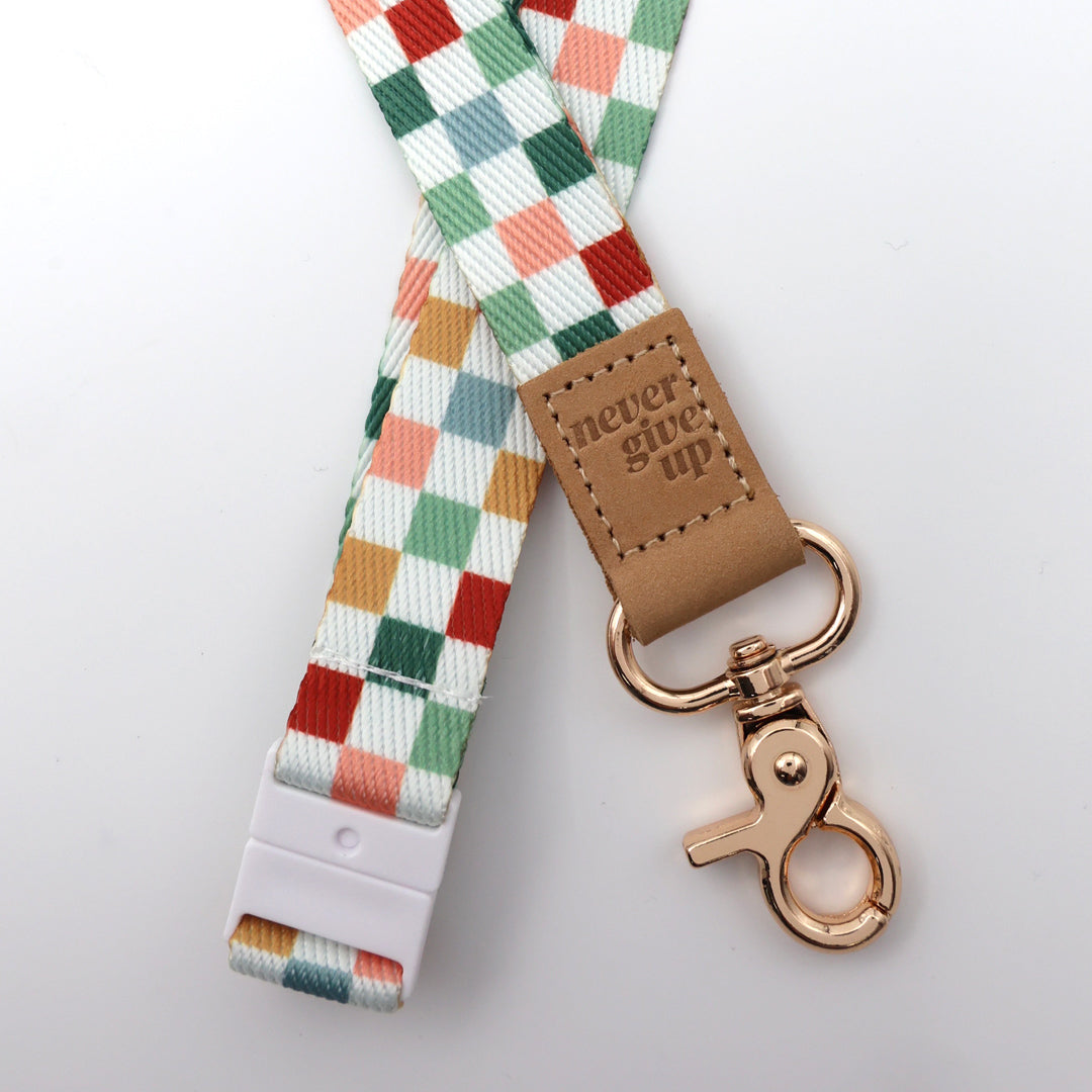 Plaid lanyard with 'never give up' tag and rose gold clip on a light gray background