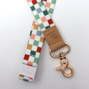 Plaid lanyard with 'never give up' tag and rose gold clip on a light gray background