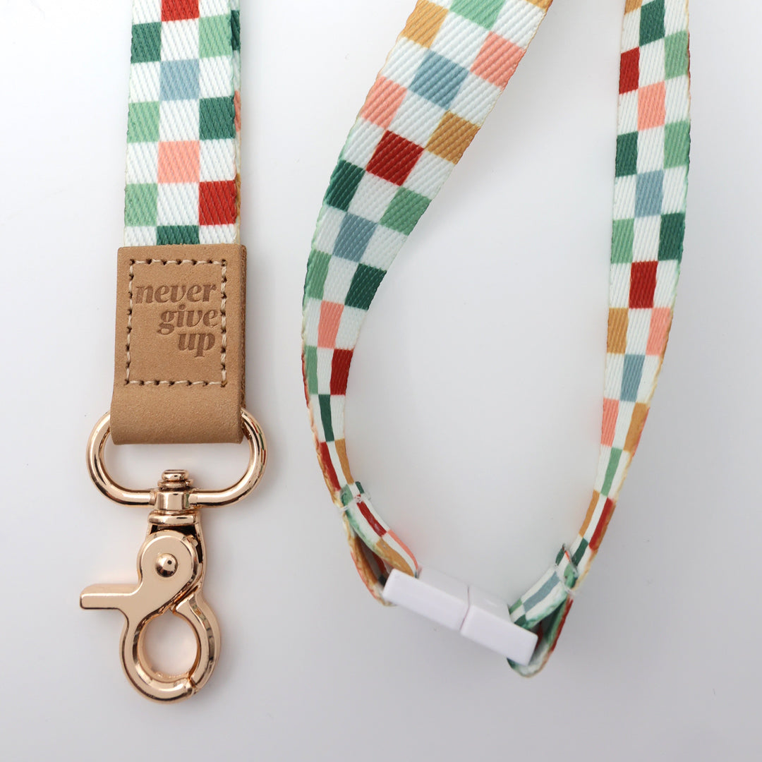 Colorful checkered lanyard with a brown leather tag and rose gold clasp on a light gray background
