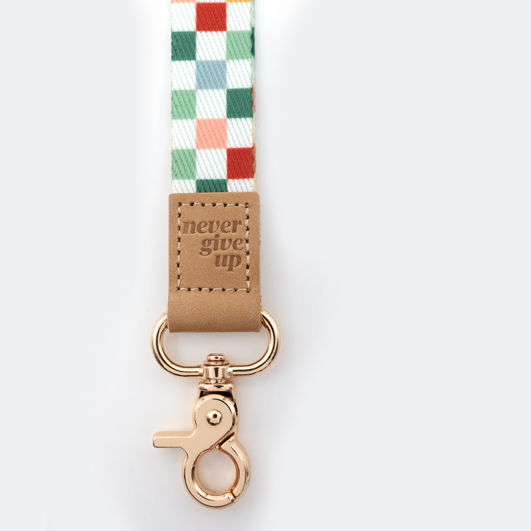 Checkered ribbon with a brown leather tag and rose gold clasp on a white background