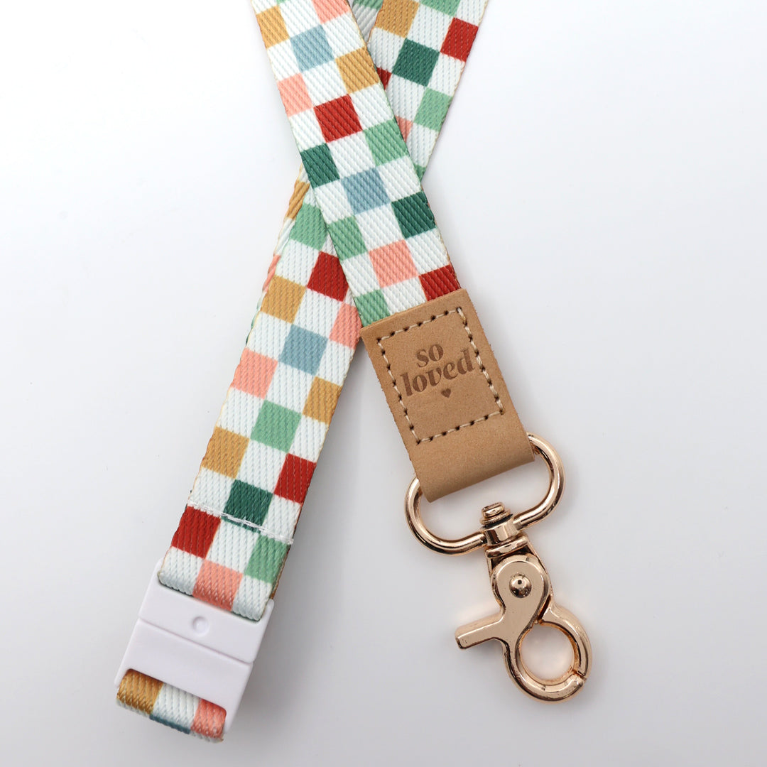 Multicolored checkered lanyard with a brown leather tag and rose gold clasp on a light gray background