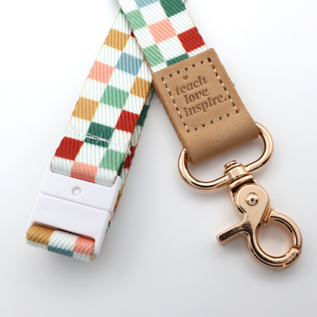Colorful checkered strap with a rose gold clasp and 'teach love inspire' tag on a white background