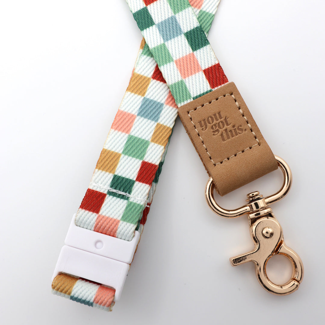 Colorful checkered strap with a brown tag and gold clasp on a light gray background