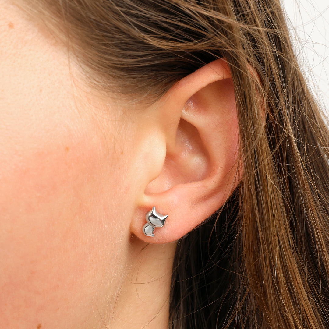 A close-up of a person's ear wearing a small silver cat stud earring.