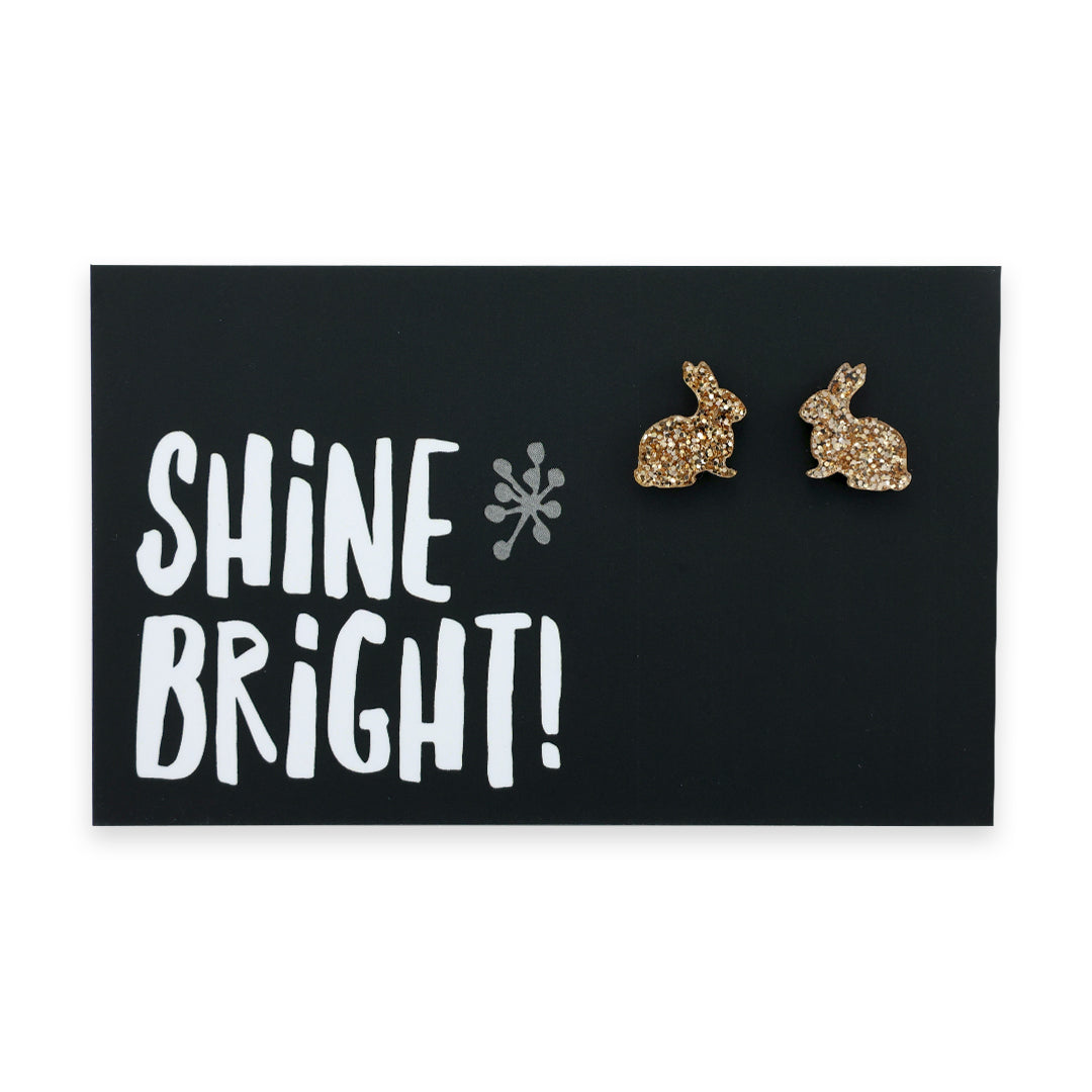 A pair of champagne gold acrylic bunny stud earrings displayed on a black card with the text 'SHINE BRIGHT!' and a star symbol.