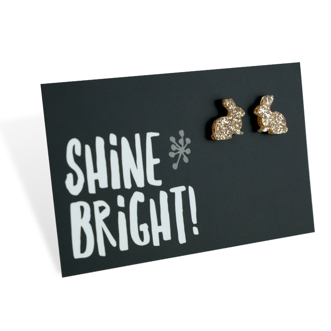 A pair of champagne gold acrylic bunny stud earrings displayed on a black card with the text 'SHINE BRIGHT!' and a star symbol.