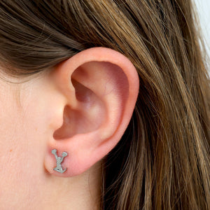 Close-up of an ear wearing a small silver earring with a 'Cheer leader shaped' design.
