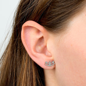 Silver earring worn by a Cheer leader shaped studs on a light gray background