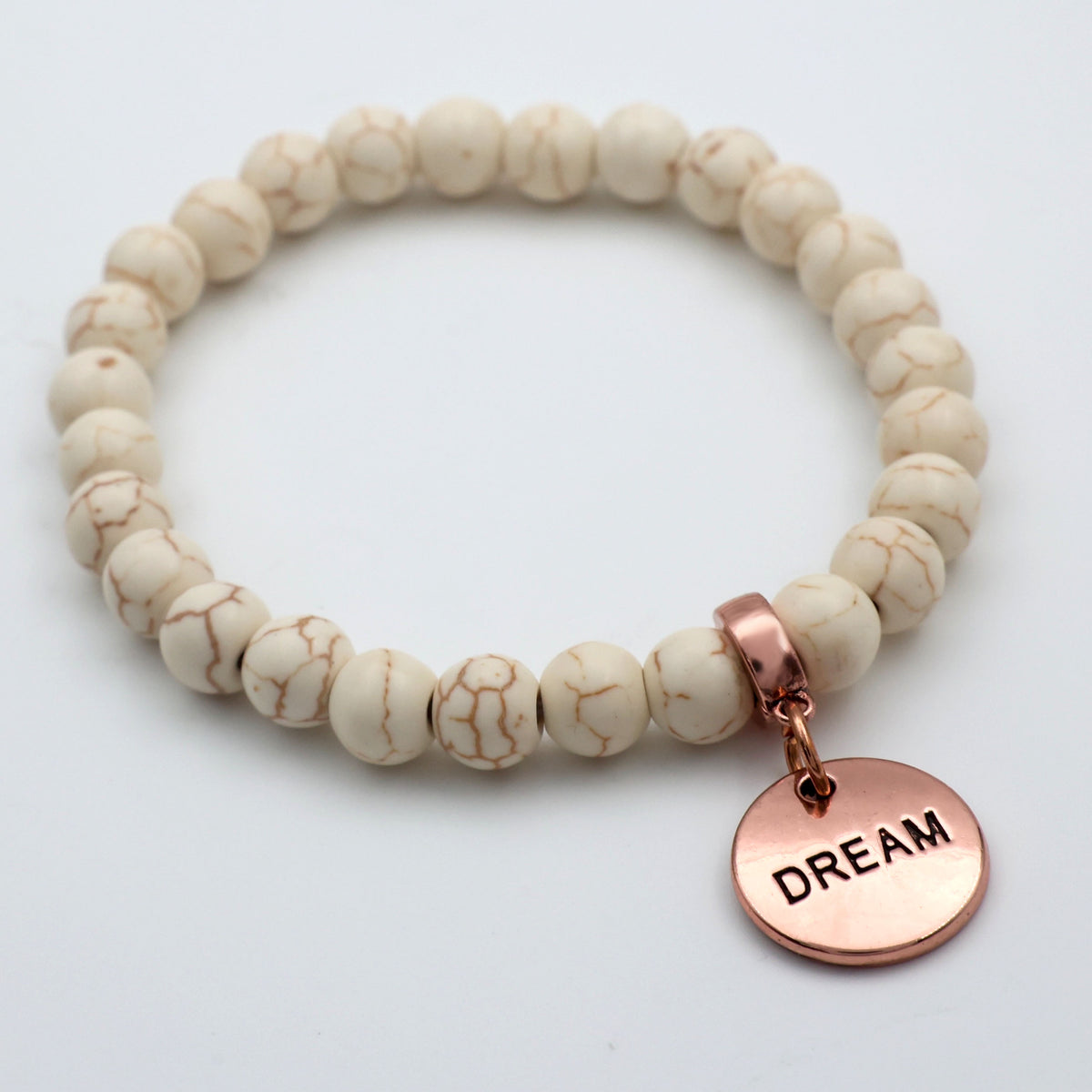 Beaded bracelet with a rose gold 'DREAM' charm on a light background