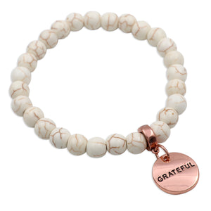 White beaded bracelet with a rose gold 'GRATEFUL' charm on a white background
