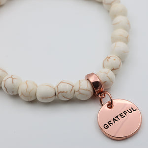 Beaded bracelet with a rose gold 'GRATEFUL' charm on a light background