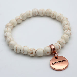 Beaded bracelet with a rose gold 'STRENGTH' charm on a light background