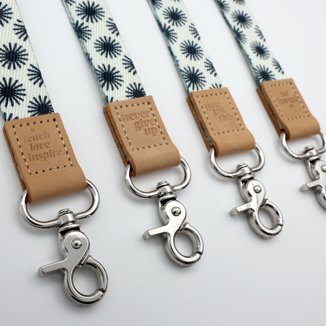 Three lanyards with floral pattern and leather tags on a light gray background