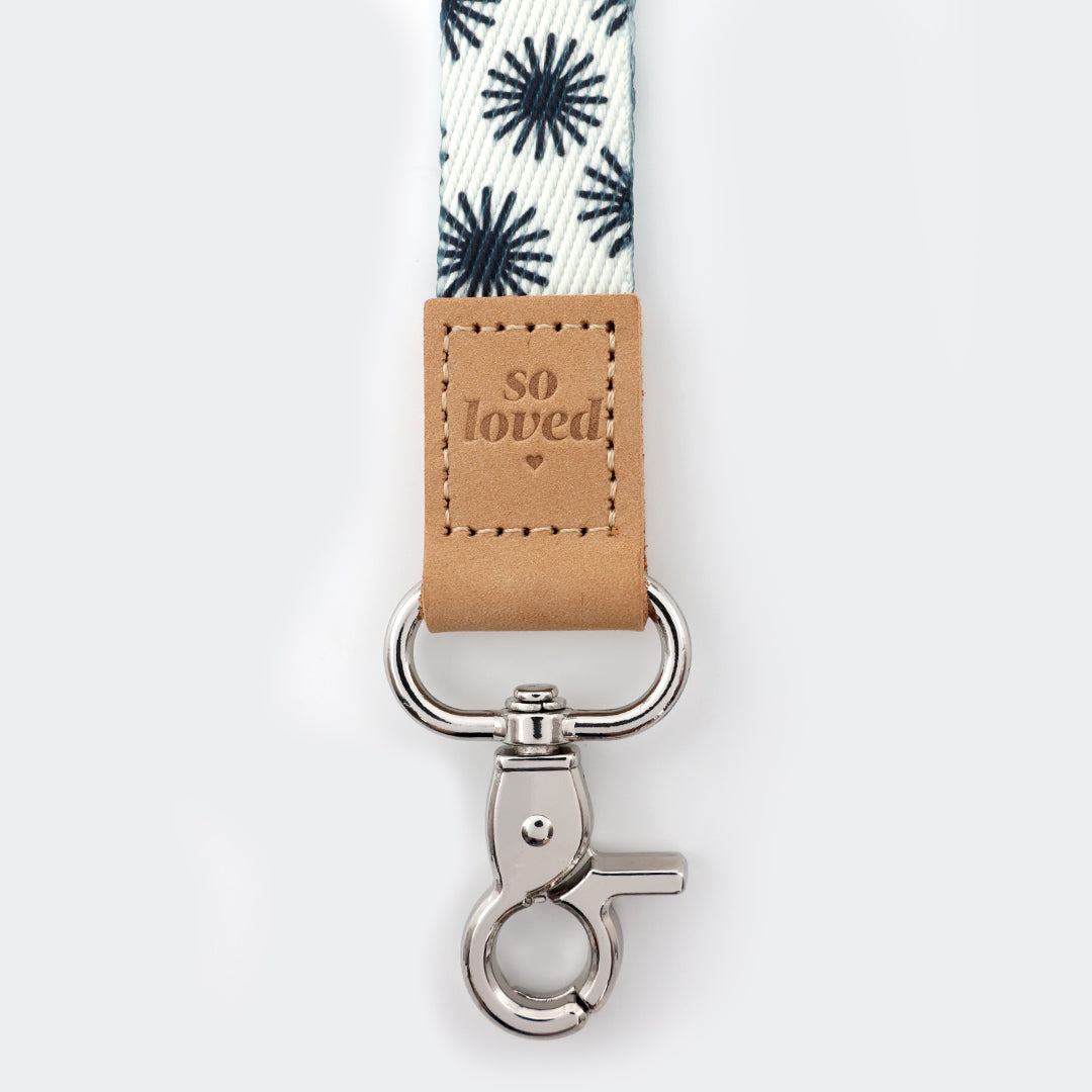 Keychain with floral-patterned strap and 'so loved' tag on a white background