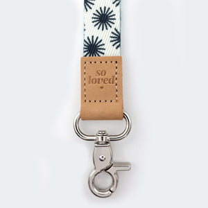 Keychain with floral-patterned strap and 'so loved' tag on a white background